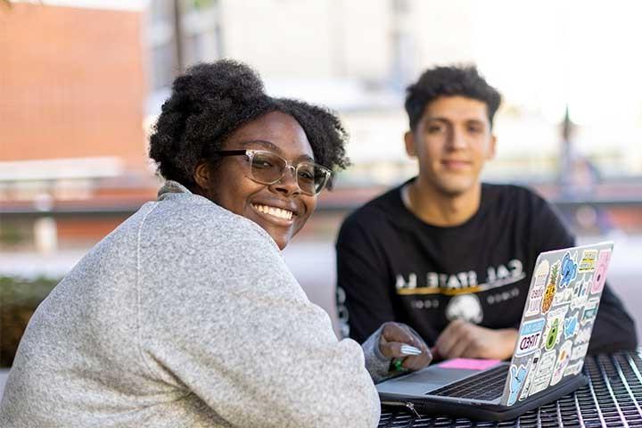 Two students smiling while studying with a laptop